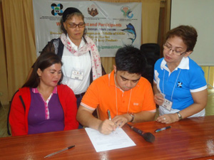 Seth Ryan Delos Reyes (center, in orange), General Manager of Super Royale Seafoods International Inc. and Ruth M. Lazarte (left, in violet) of the Balingasag Producers Cooperative signing the Memorandum of Understanding (MOU). Dr. Dalisay DG. Fernandez (right, in blue), IARRD-PCAARRD Director and a member of the cooperative served as witnesses. (Image credit: IARRD, PCAARRD)